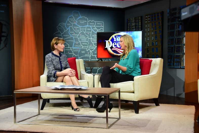 Prof. Susan Roberts on Fox Carolinas sits on a chair on a TV set, across from host