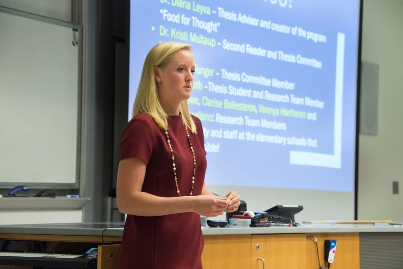 Student stands in front of screen in a lab giving a presentation