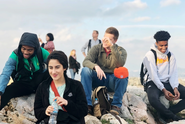 Four students sit on rocks at the Acropolis laughing