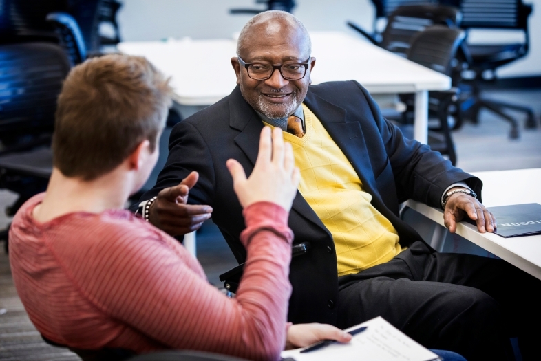 Robert Bullars smiles while a student sitting next to him discusses economics