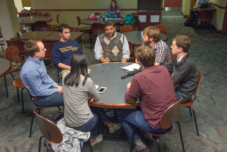 Professor and six students sit around a round table in the Union discussing economics