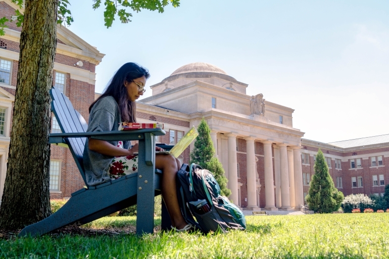 Student sits on outdoor chair on Chambers Lawn and does classwork