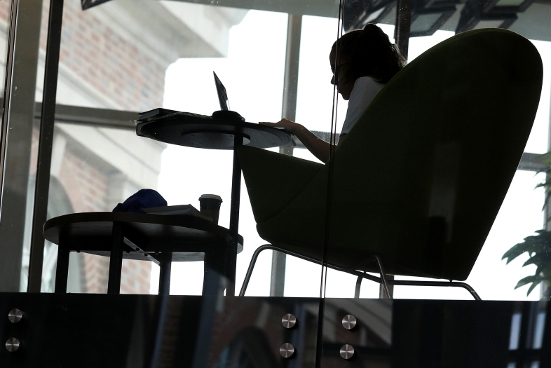 Student studies in the Wall Center sitting in an oversized chair by the window