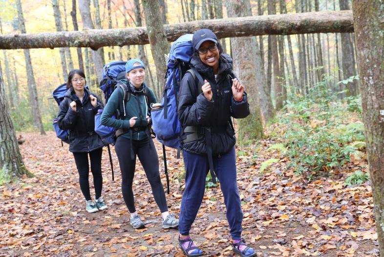 Three students backpacking in the woods walk in a line