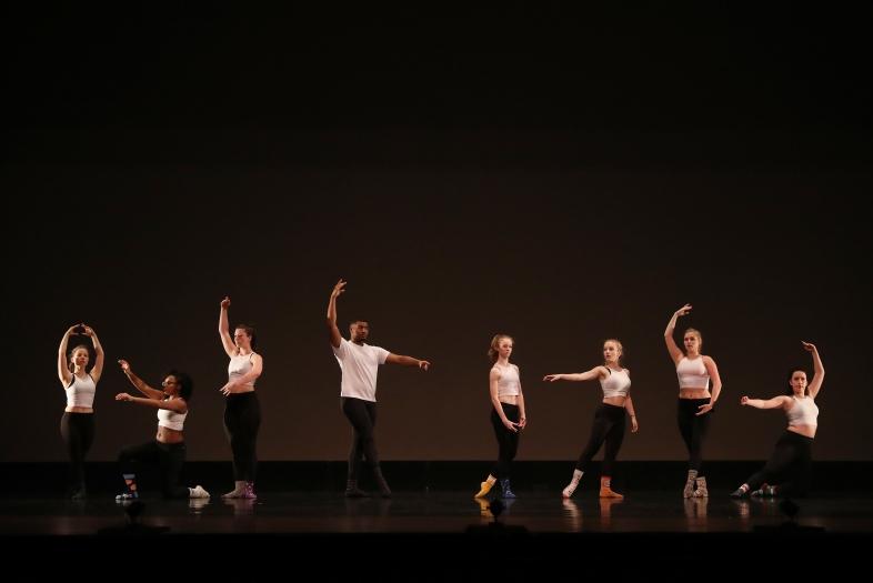 Dancers on stage take different positions in front of a black background