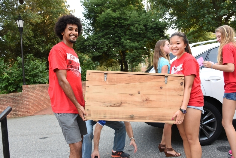 Two students carry a big trunk inside during move in day