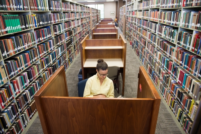 Student sits in carrel surrounded by books