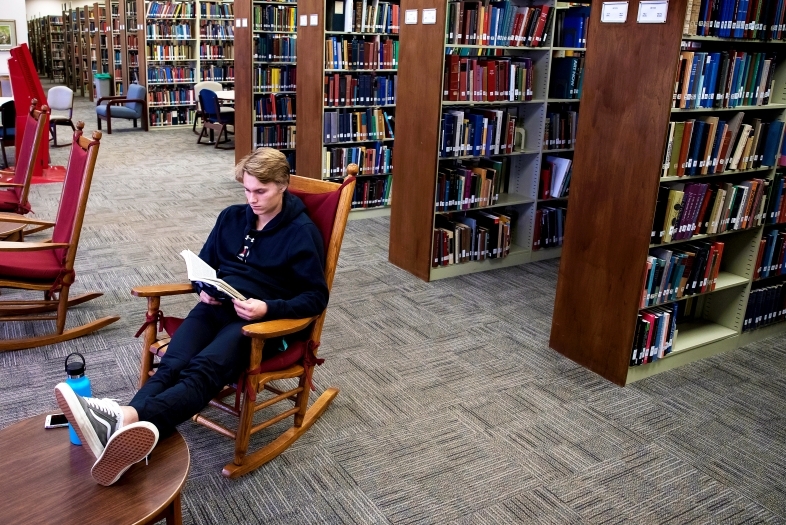 Student Reads Book in Library Rocking Chair