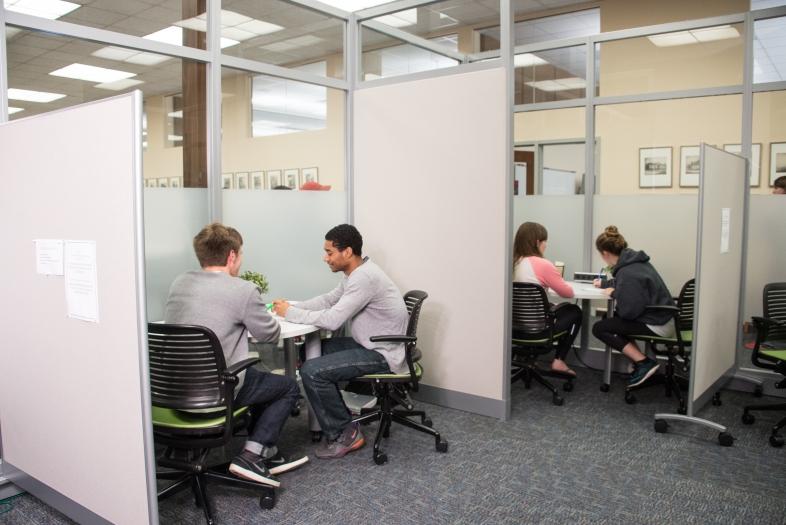 Two sets of students meet in glass cubicles with student writing tutors