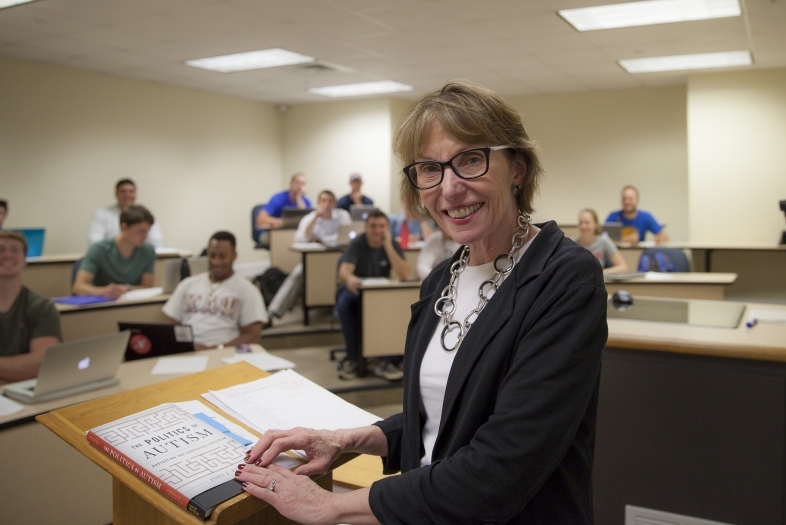 Prof. Roberts smiles at camera while leading class from podium