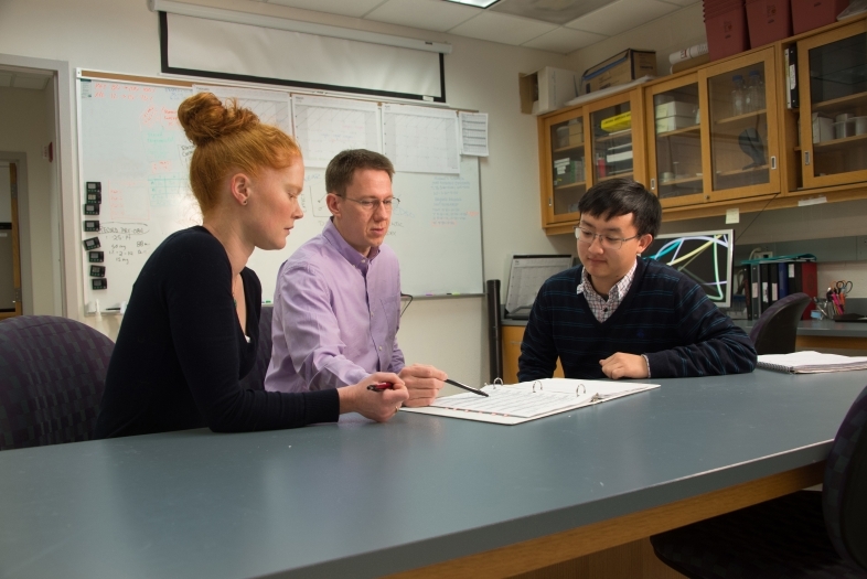 Mark Smith and two students sit around lab table and analyze data