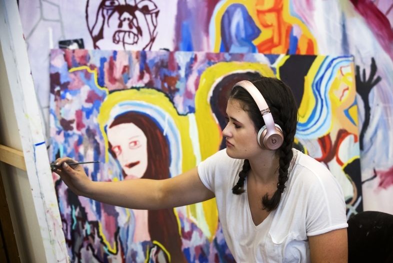 Student painting & surrounded by canvases