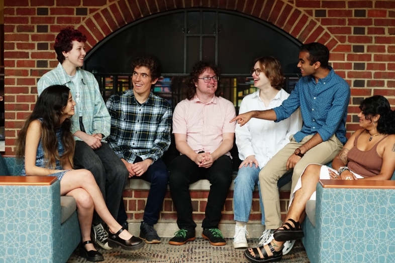 seven students sitting around a fireplace together talking and smiling