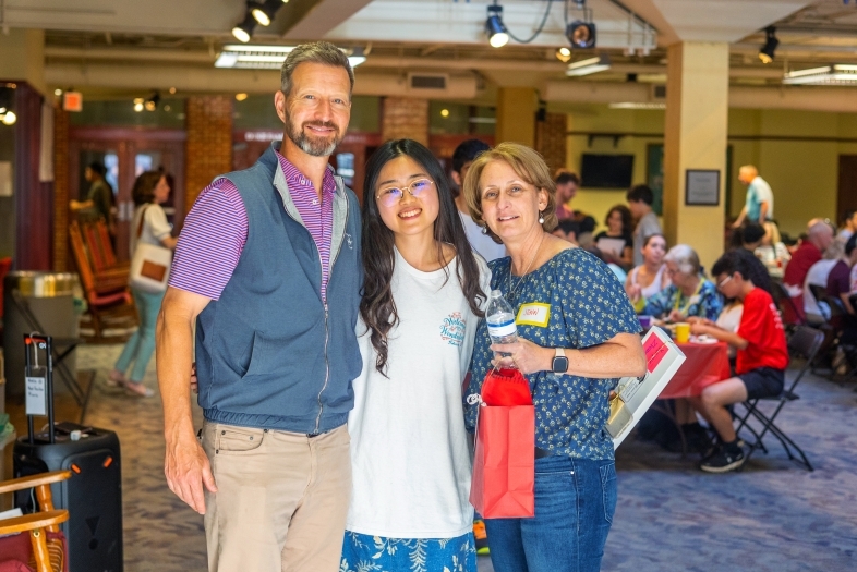 Two adults with a student smiling with tables and chairs in background