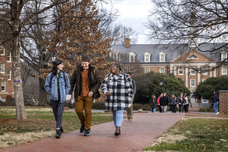 Three students walk together on campus and smile at each other