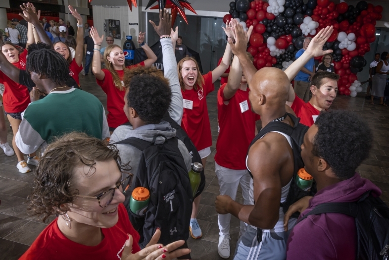 A group of students in red shirts cheer and welcome new students 