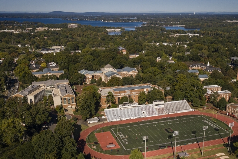 an aerial view of Davidson College campus with a football field in the foreground and a lake in the background