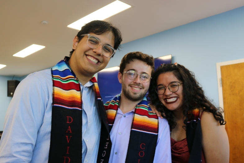 three Latinx students smile together while wearing graduation stoles