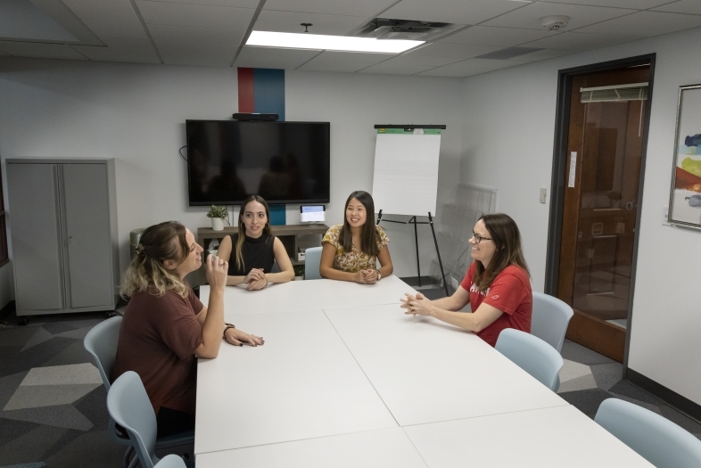 a group of four women sit around a conference table talking