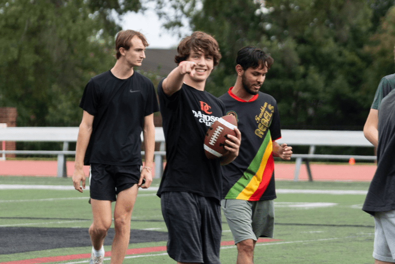 a group of young men holding a football and smiling while standing on a football field