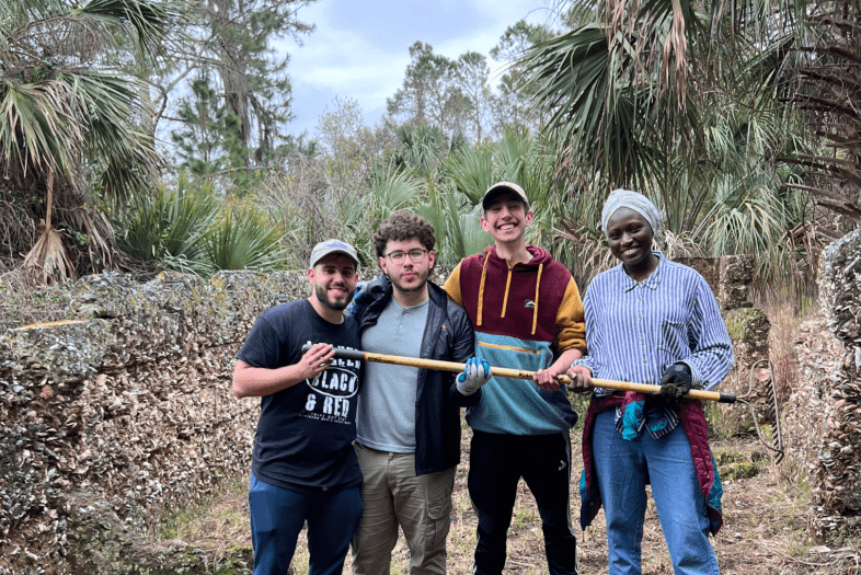 a group of four young people hold a wooden tool in a tropical scene