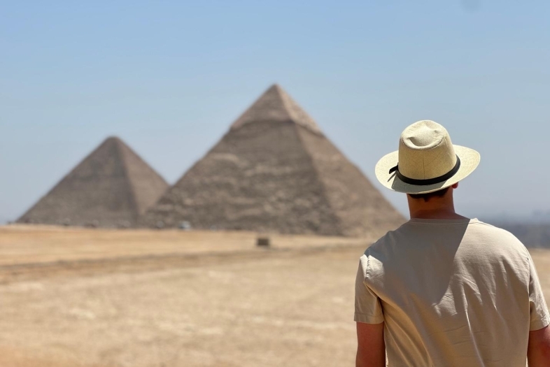 a young man stands in front of the Egyptian pyramids