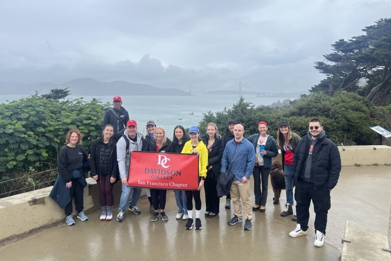 Group of Davidson alums outdoors with branded flag