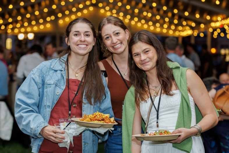 a group of three young women holding plates of food and smiling