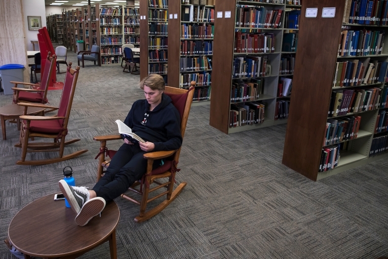 a young person reads a book in a rocking chair in a library