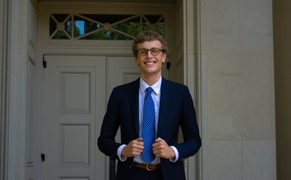 a young white man wearing a suit and tie standing in front of an old building