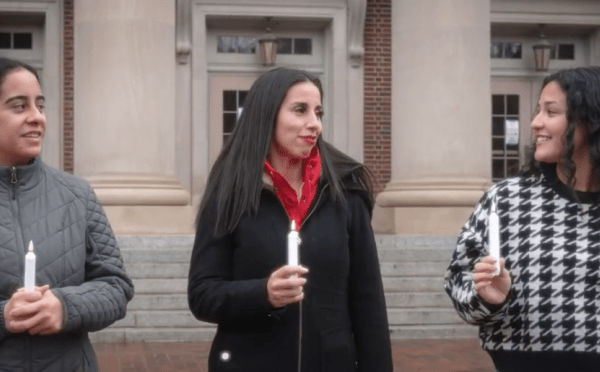 three young women walk together talking and holding candles