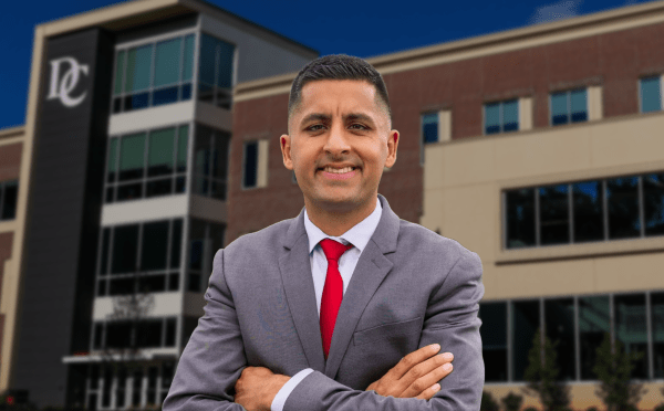 a young man stands in front of a stadium wearing a suit and red tie