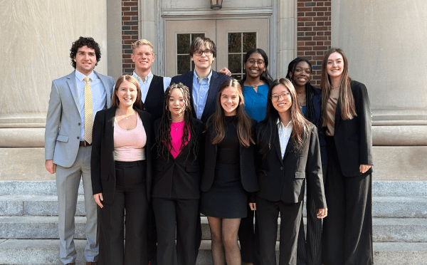 a group of young people in business formal clothing standing together in front of an academic building