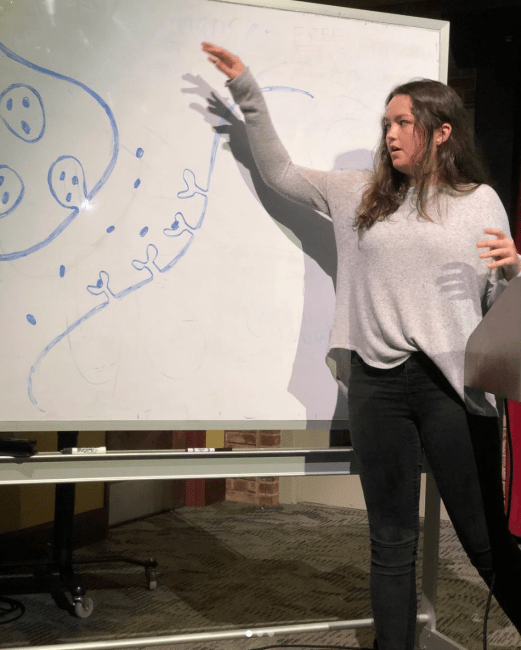 Student gives presentation while pointing to whiteboard drawing