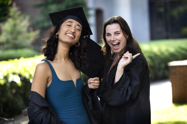 two graduates in cap and gown pose smiling