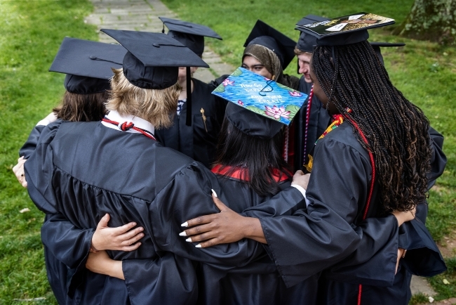 Group of students in caps and gowns huddled up and smiling