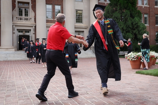 Student high-fiving an adult while wearing graduation regalia