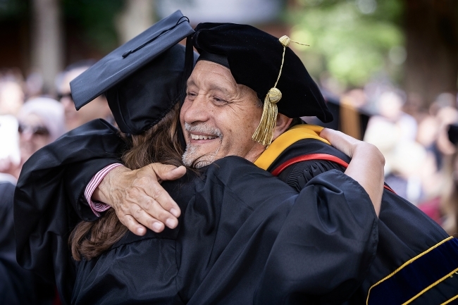 Professor and student hug while wearing commencement regalia