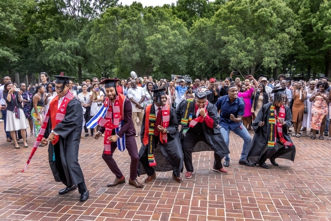 Men in caps and gowns pose after graduation ceremony