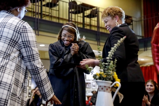 Three women smile and embrace while wearing graduation regalia