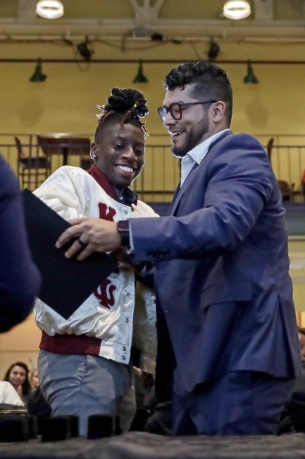 Two men hug and smile while holding a diploma