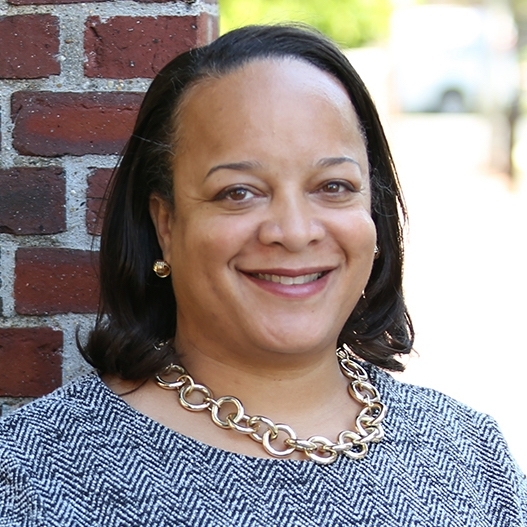 A woman smiling wearing a herringbone dress and a gold necklace