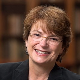 A white woman with short brown hair smiles and wears glasses