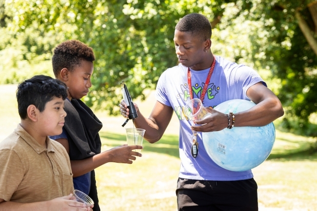 A student stands with two kids holding a ball