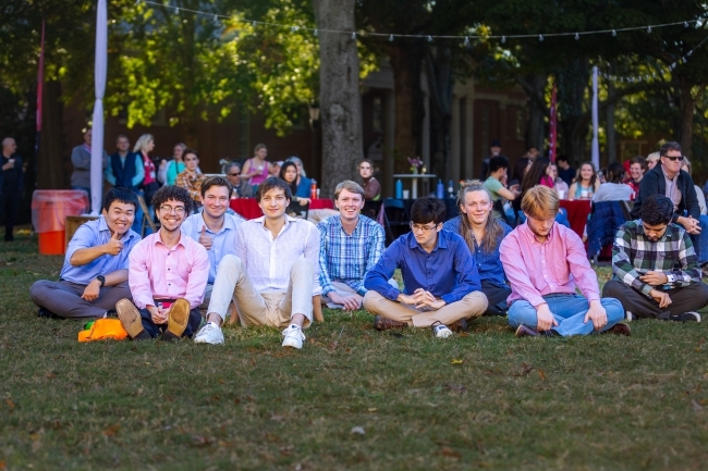 a group of students sitting on a grassy lawn and smiling