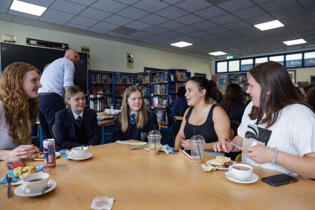 a group of college aged and middle school students sit around a table eating and talking