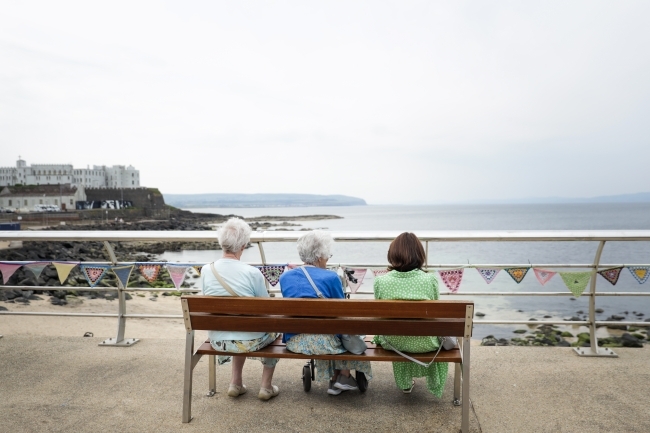 a group of three women sit on a bench overlooking the sea