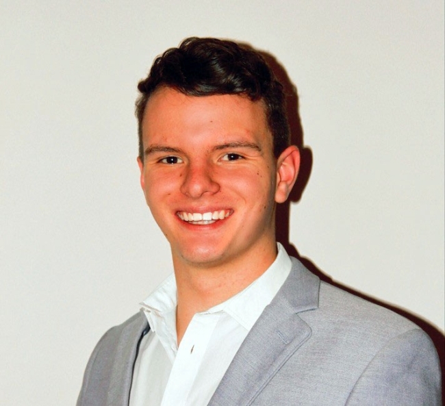 a young white man wearing a collared shirt and jacket while smiling