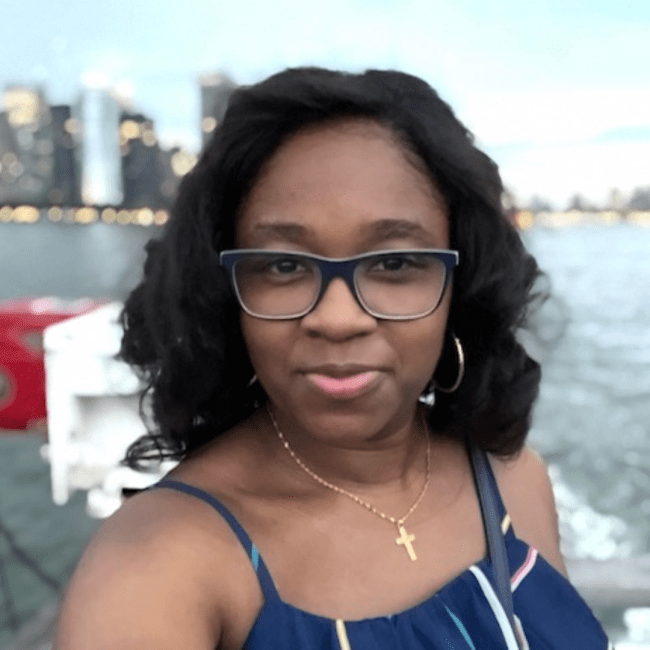 a young Black woman wearing a sundress and standing in front of a body of water and skyscrapers