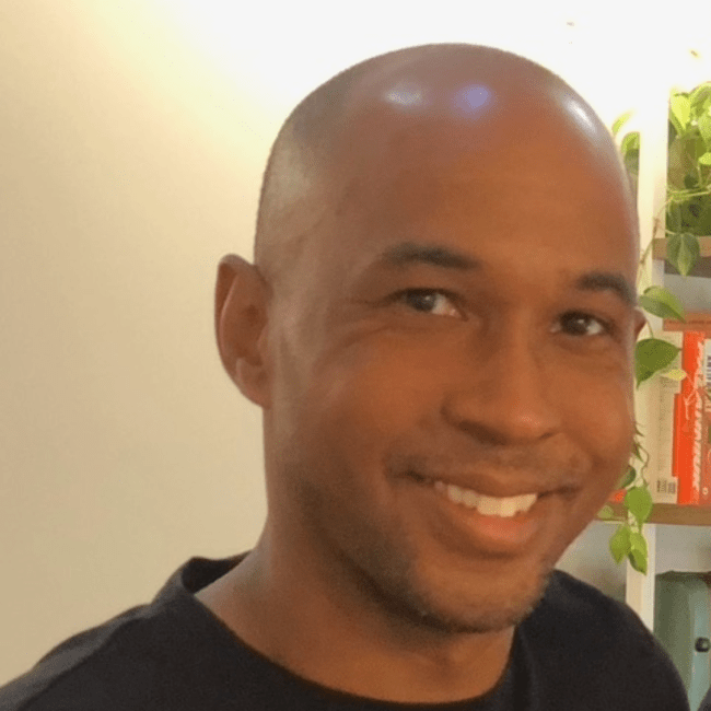 a young Black man smiles while wearing a black shirt